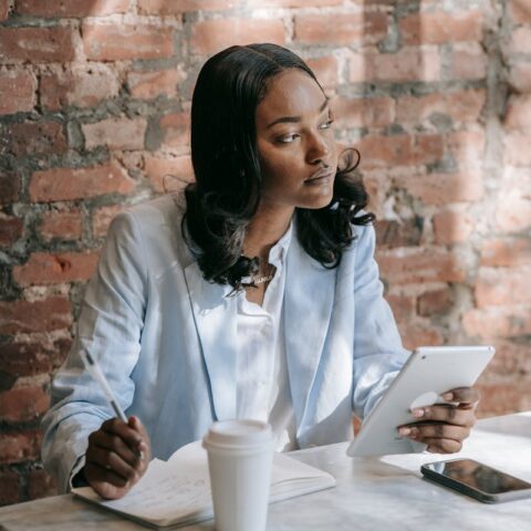 Une femme d'affaires noire dans un café, utilisant pensivement une tablette pendant son travail.