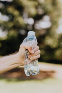 Recadrer un homme méconnaissable froissant une bouteille d'eau en plastique à la main sur un fond flou d'arbres verts du parc lors d'une journée d'été ensoleillée