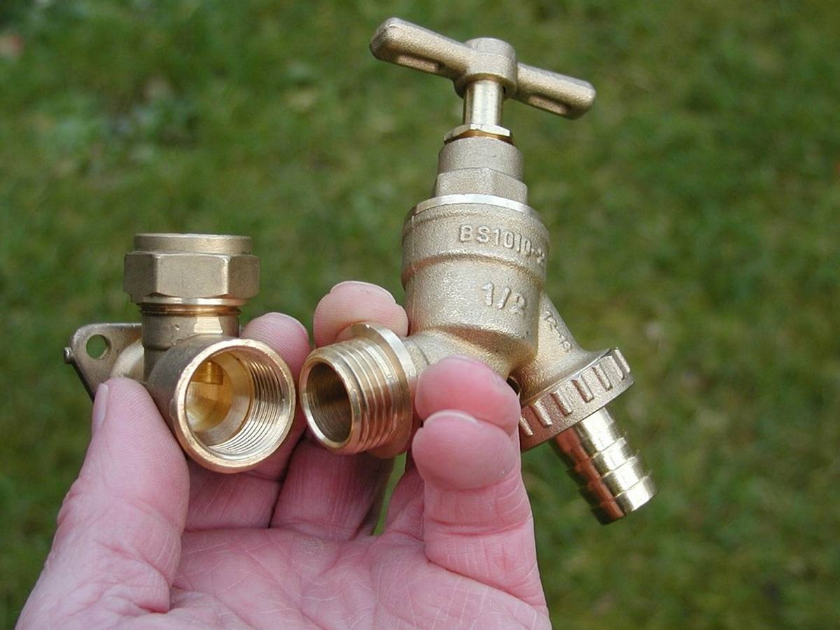Main tenant des raccords et un robinet en laiton sur fond d'herbe