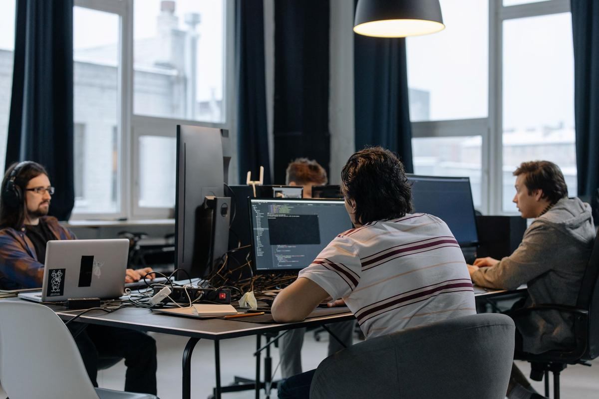 Bureau de développeurs informatiques avec écrans, ordinateurs portables et grande baie vitrée sur ville