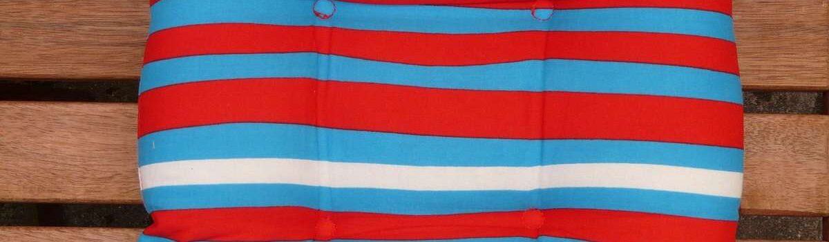 Coussin rayé rouge, bleu et blanc posé sur banc en bois