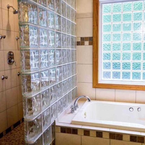 Salle de bain avec baignoire blanche, douche, et fenêtre en carreaux de verre coloré