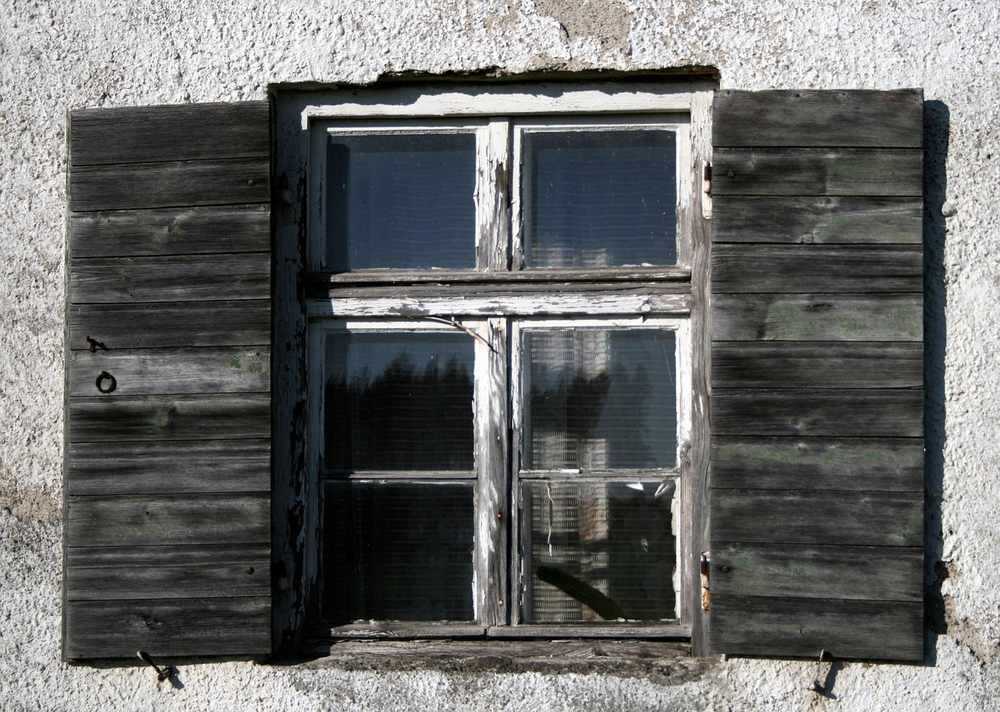 Fenêtre à volets grisâtres sur façade de ciment, quatre vitres divisées en deux étages