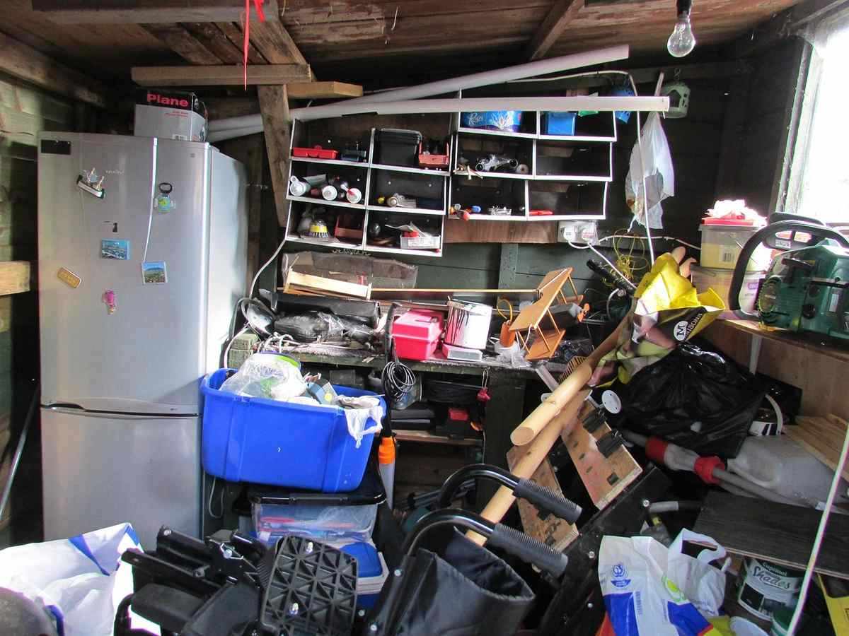Un garage encombré avec réfrigérateur, étagères, outils et matériel divers